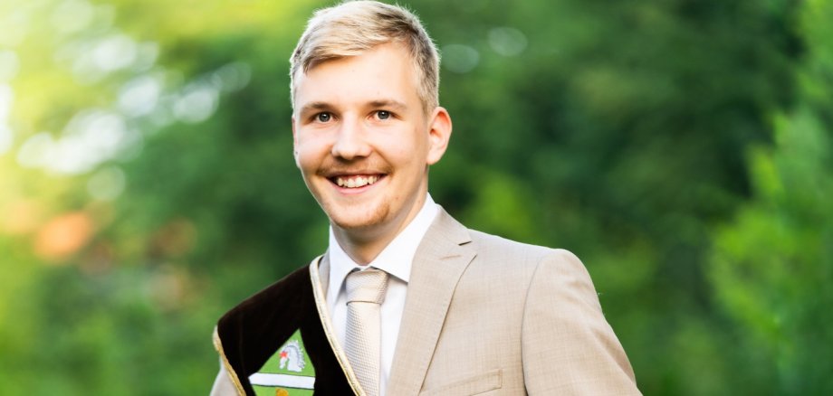 Kartoffelkönig Georg Röhrs Portraitfoto des Kartoffelkönigs Georg Röhrs. Ein junger, blonder lächelnder Mann in beigem Anzug und einer braunen Scherpe mit der Aufschrift "Neuenkirchener Kartoffelkönig"