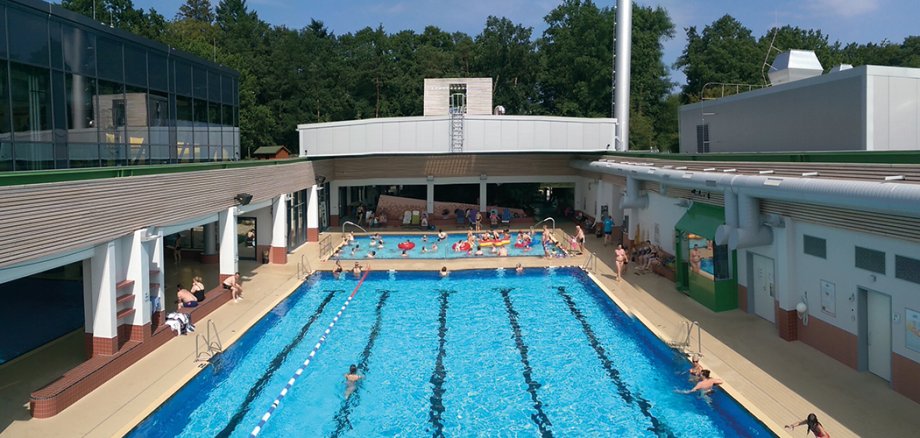 Blick von oben auf das Schwimmbecken der Soltau Therme. Das Cabrio-Dach ist geöffnet. Menschen schwimmen im Wasser.