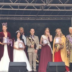 7 Gasthoheiten und Kartoffelkönig Tjarc-Ole auf der Festbühne zum Kartoffelfest 2024. Alle in ausgefallenen Kostümen und Kleidern; Geschenke in der Hand